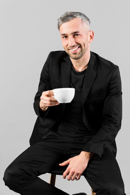 Man in black suit holding a small cup of tea