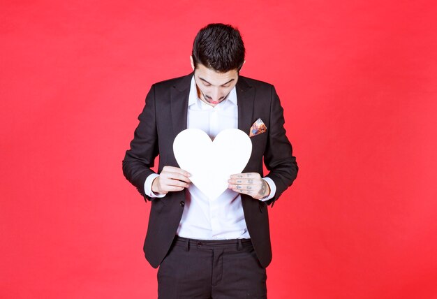 Man in black suit holding a white heart .