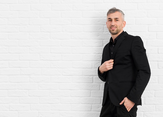 Man in black suit leaning on a wall