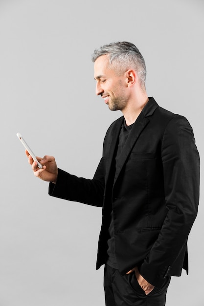 Foto gratuita uomo in abito nero lateralmente guardando il telefono