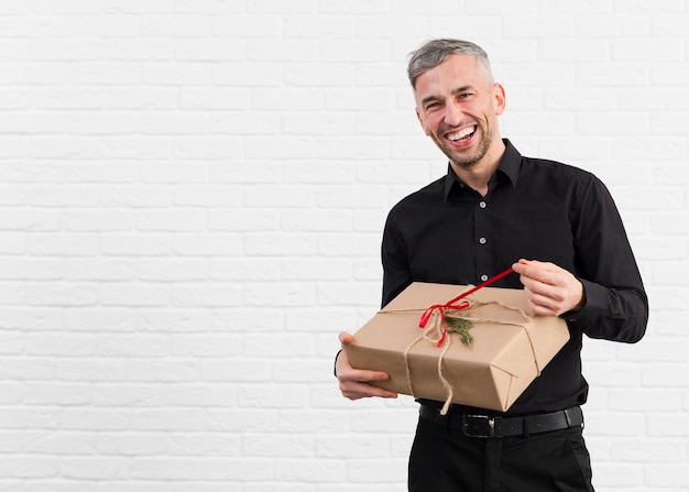 Мужчина в черном костюме распаковывает подарок и улыбается