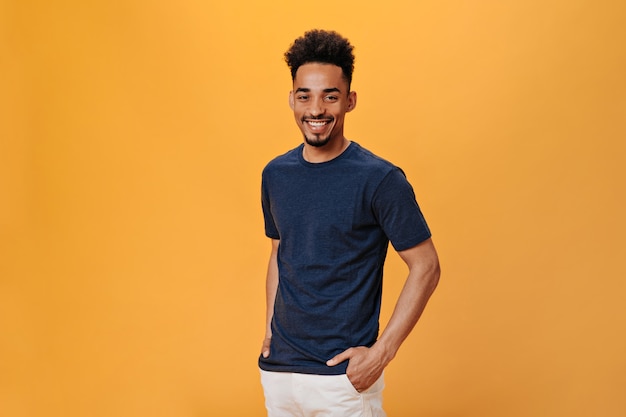 Man in black t-shirt smiles sweetly on orange wall