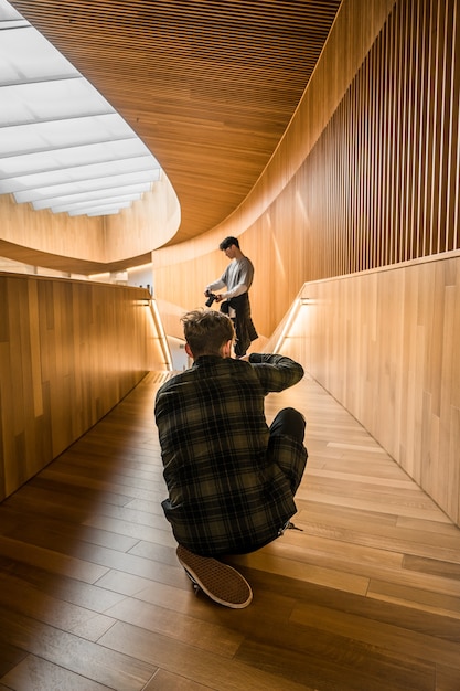 Man in black and white plaid dress shirt sitting on brown wooden floor taking a photo