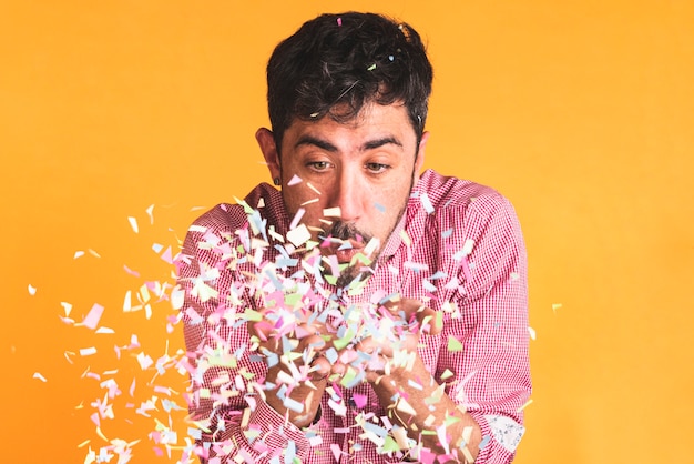 Free photo man blowing confetti on orange background