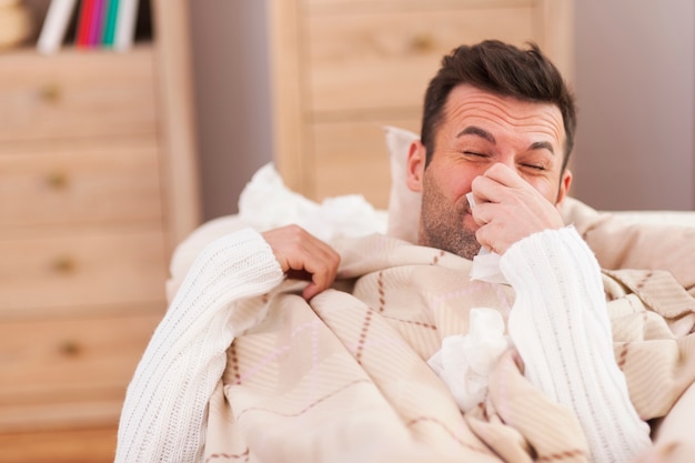 Man blowing his nose in bed
