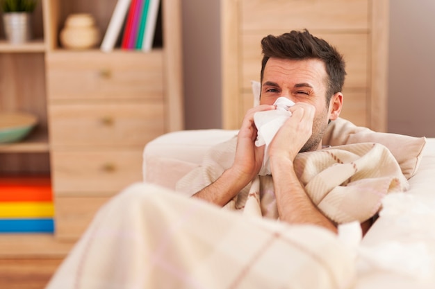 Man blowing his nose while lying sick in bed