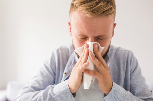 Man blowing nose with eyes closed