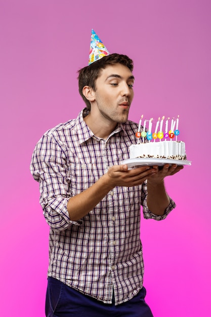 Man blowing out candles on birthday cake over purple wall.