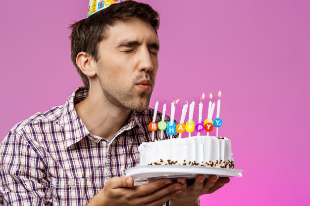Человек, выдува свечи на день рождения торт над фиолетовой стеной.