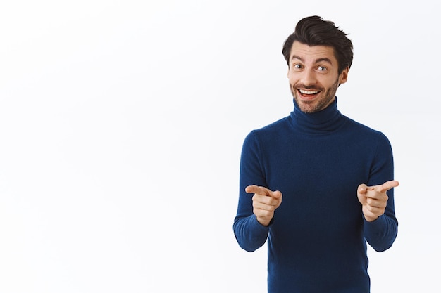 青いハイネックのセーターを着た男が、カメラを指差して喜んで笑顔で、会議中に雇用主を励ます