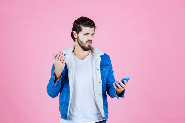 Man in a blue jacket looking to his phone with surprize. 