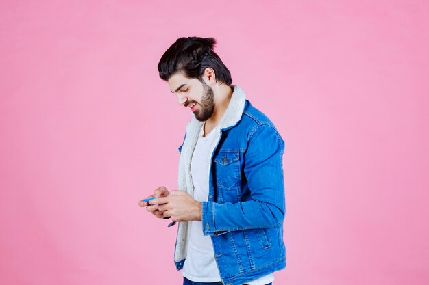 Man in blue jacket writing message or commenting on the phone. 