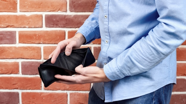 Free photo man in blue shirt showing black empty wallet