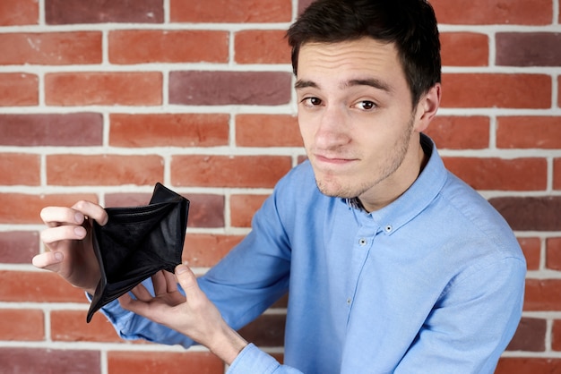 Foto gratuita uomo in camicia blu che mostra portafoglio vuoto nero