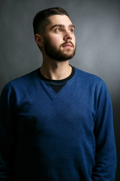 Man in blue sweater stands straight holding his head up 