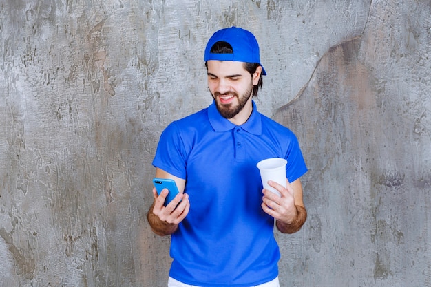 Free photo man in blue uniform holding a takeaway drink and making a video call.