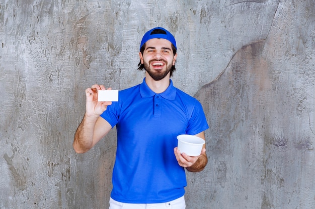 持ち帰り用のプラスチック製のコップを持って名刺を提示する青い制服を着た男。