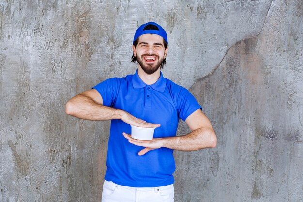 Man in blue uniform holding a takeaway plastic cup . 