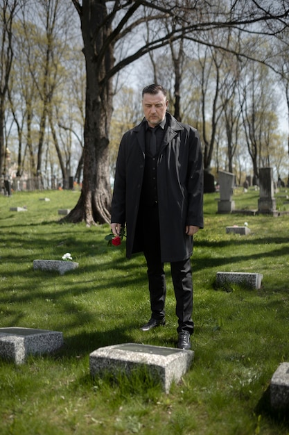 Man bringing a rose to a tombstone at the cemetery