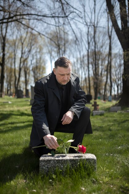 Man bringing a rose to a tombstone at the cemetery