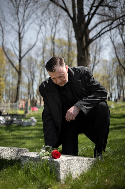 Man bringing a rose to a tombstone at the cemetery