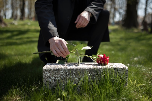 Мужчина приносит розу к надгробной плите на кладбище