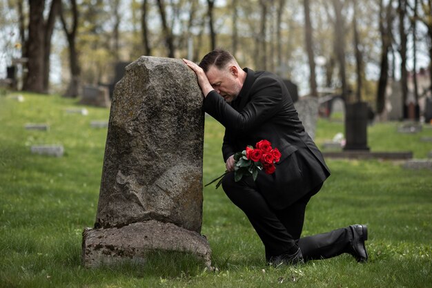 Мужчина приносит розы к могильному камню на кладбище