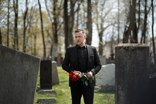 Free photo man bringing roses to a gravestone at the cemetery