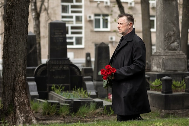 Free photo man bringing roses to a gravestone at the cemetery