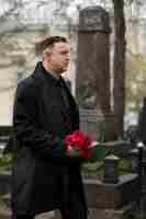 Free photo man bringing roses to a gravestone at the cemetery