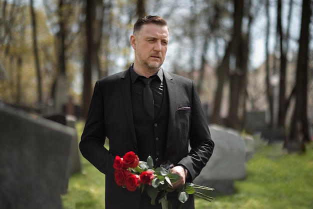 Free photo man bringing roses to a gravestone at the cemetery