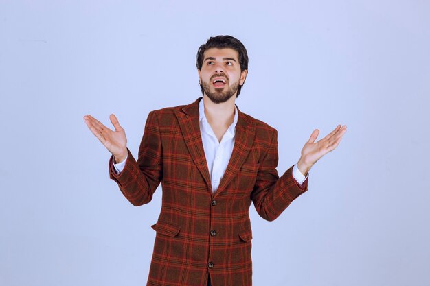 Man in brown blazer having speech with wide opening his hands. 