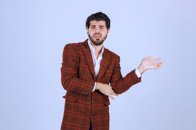 Man in brown blazer pointing and introducing something on the right.