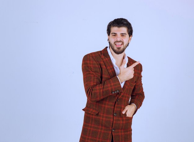 Man in brown blazer pointing right and speaking. 