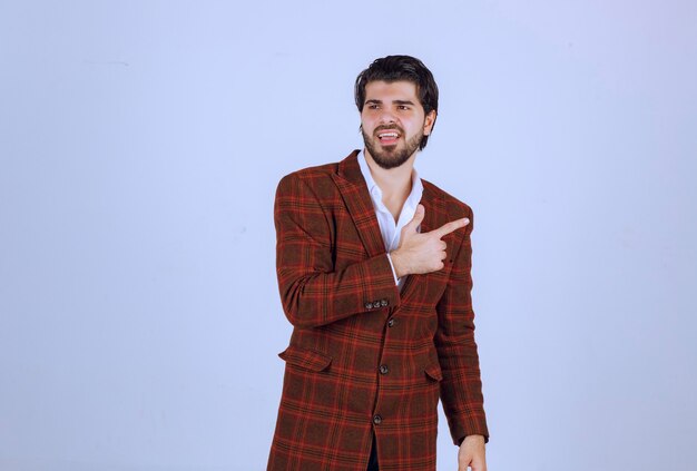 Man in brown blazer pointing right and speaking. 