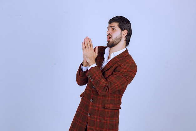 Man in brown blazer uniting his hands and praying. 