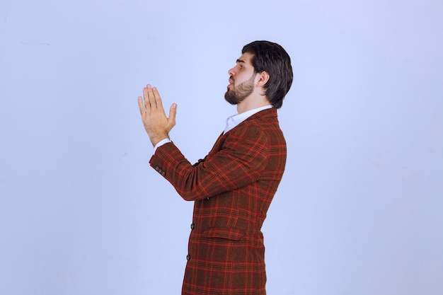 Uomo in giacca sportiva marrone unendo le mani e pregando.