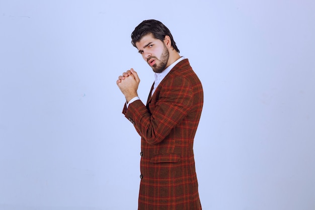 Man in brown blazer uniting his palms and asking for something. 