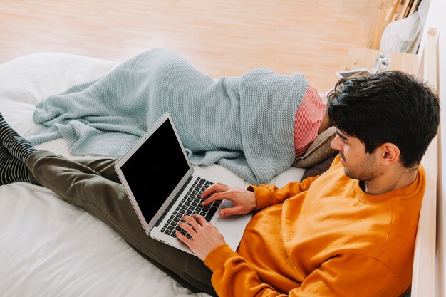 Man browsing laptop near sleeping woman