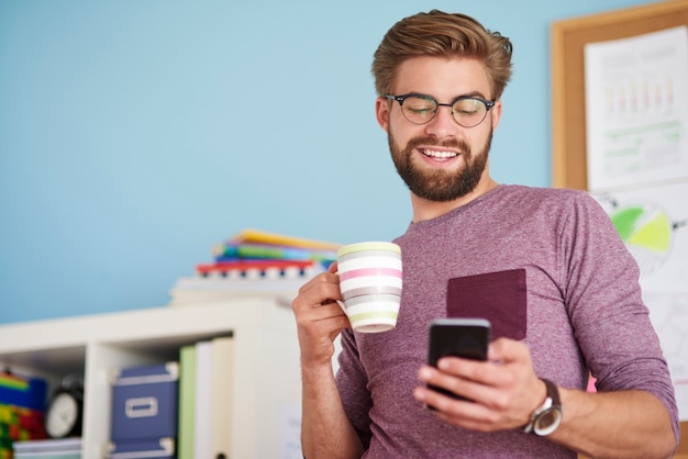 携帯電話を閲覧し、コーヒーを飲む男