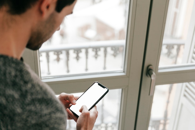 Free photo man browsing smartphone near window