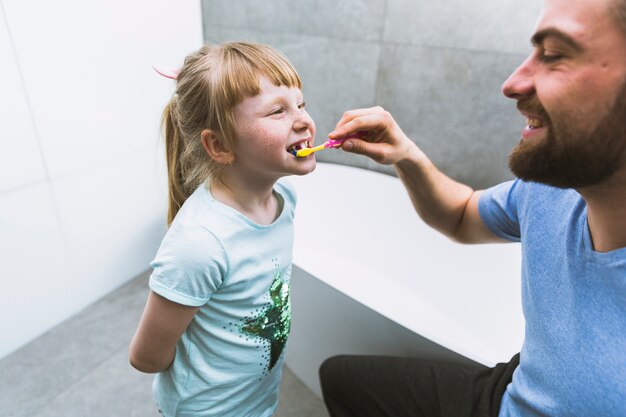 Man brushing teeth of daughter