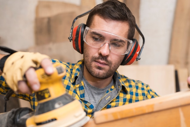 Foto gratuita il carpentiere del costruttore dell'uomo lucida il bordo di legno con una levigatrice orbitale casuale