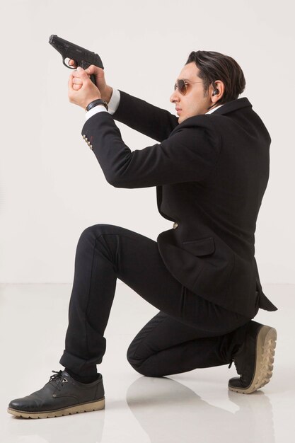 Man in business suite and gun on white background, shooting and sitting on white background