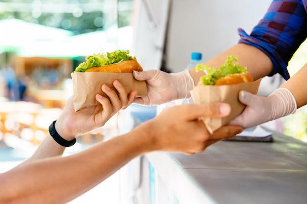 屋外で2つのホットドッグをキオスクで購入している男性。屋台の食べ物。クローズアップビュー。