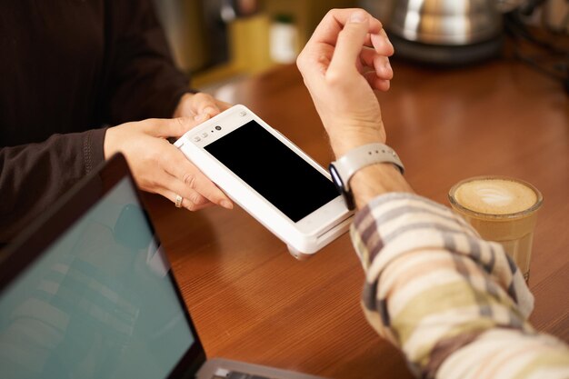 Мужчина в кафе платит бесконтактно, используя свои цифровые часы на запястье, держа их рядом с полом.