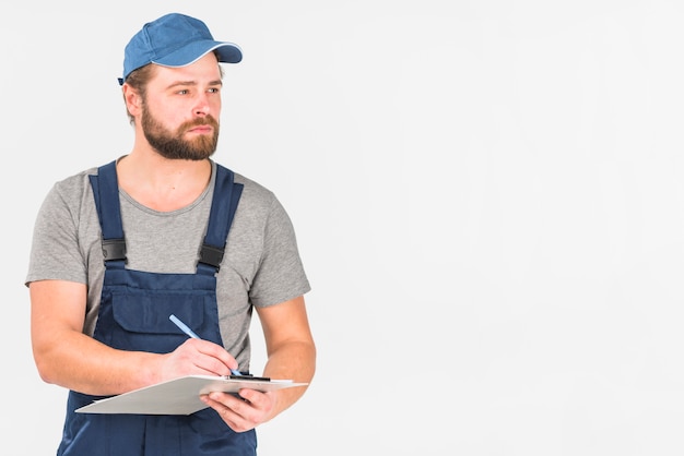 Man in cap and overall writing on clipboard 