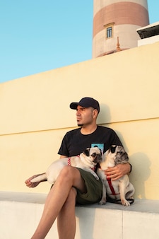 Man in a cap and sunglasses with his dogs at sunset next to the aveiro lighthouse in portugal