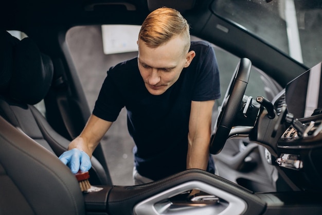 Мужчина убирает машину с помощью щетки, чтобы очистить все детали внутри автомобиля