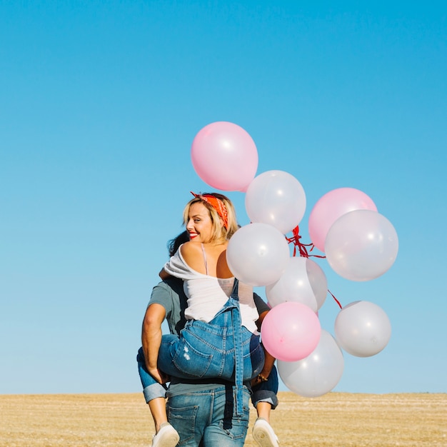 Man carrying cheerful woman with balloons
